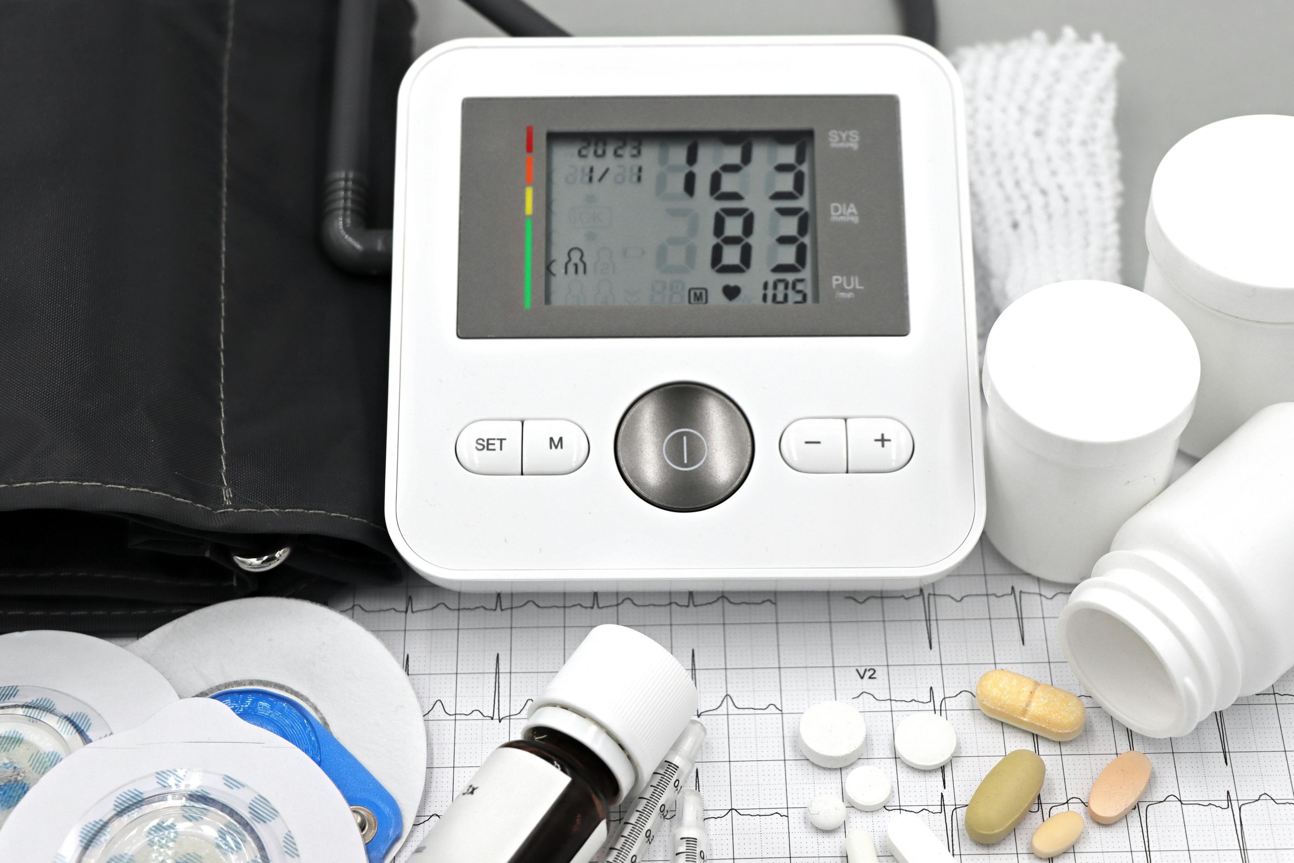 Close-up of medical equipment including blood pressure monitor, pills, and ECG printout.